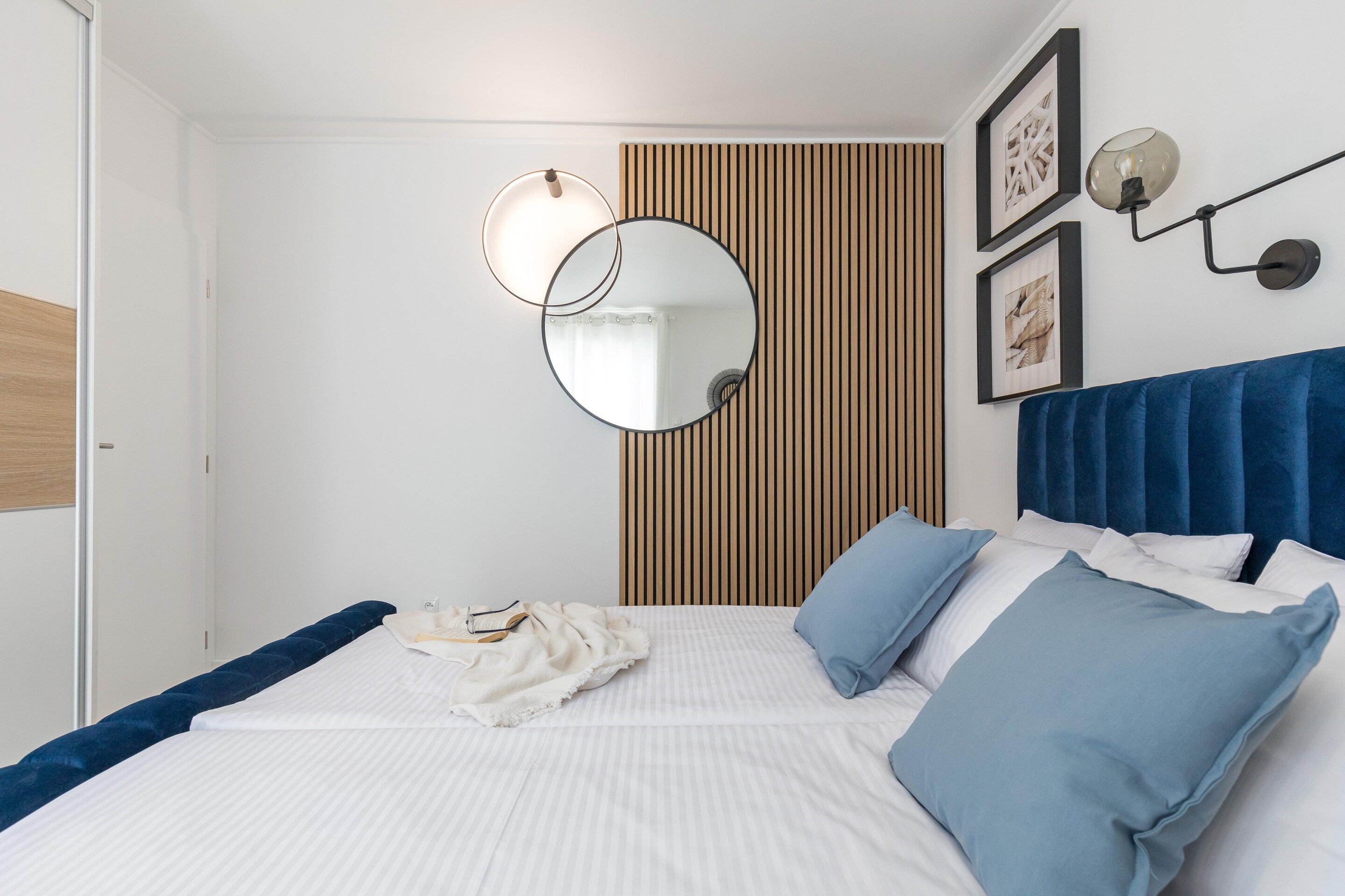 Une chambre à coucher comprenant un lit, une table de chevet, un miroir et un luminaire fixé au mur.