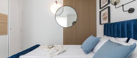 Une chambre à coucher comprenant un lit, une table de chevet, un miroir et un luminaire fixé au mur.