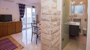 Una sala de estar moderna con una pared de acento de piedra, un comedor con mesa y sillas, y un baño con cabina de ducha de vidrio.