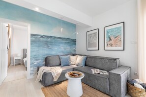 A living room with a grey sofa, a white coffee table, and a beach-themed mural on the wall. - Holiday Apartment With a Private Terrace & Hot Tub, Near the Beach (Split)