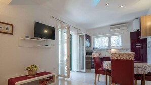A modern kitchen with a dining area, a TV mounted on the wall, and a sliding glass door leading to a balcony.