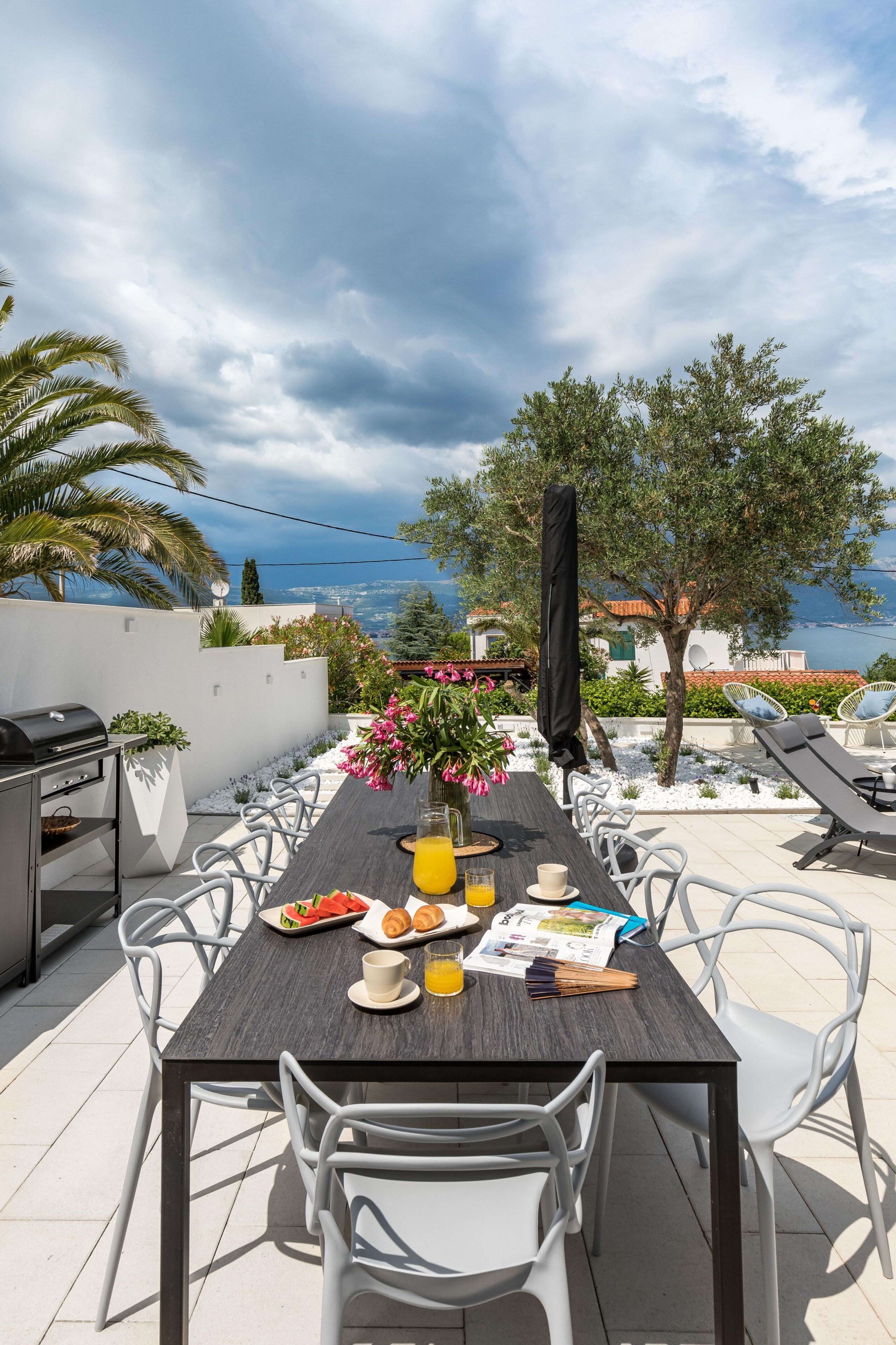 Un área de comedor al aire libre con una mesa preparada para dos, una parrilla y vista al mar.