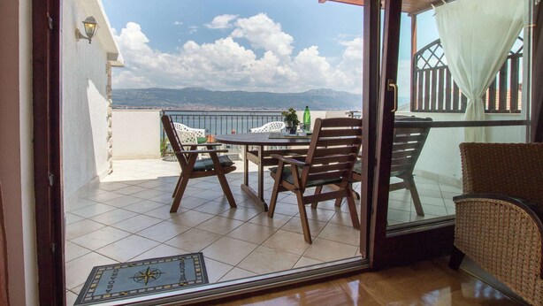 Un balcon avec une table et des chaises, une vue sur la mer et les montagnes, et un plafond orné de dentelle.