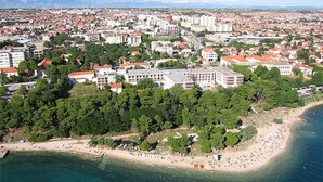 Une vue aérienne d’une ville côtière, avec une grande plage, des immeubles urbains denses et un mélange de bâtiments résidentiels et commerciaux.