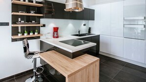 Une cuisine moderne dotée d’un îlot central, de meubles de rangement noirs et blancs et d’un luminaire suspendu.