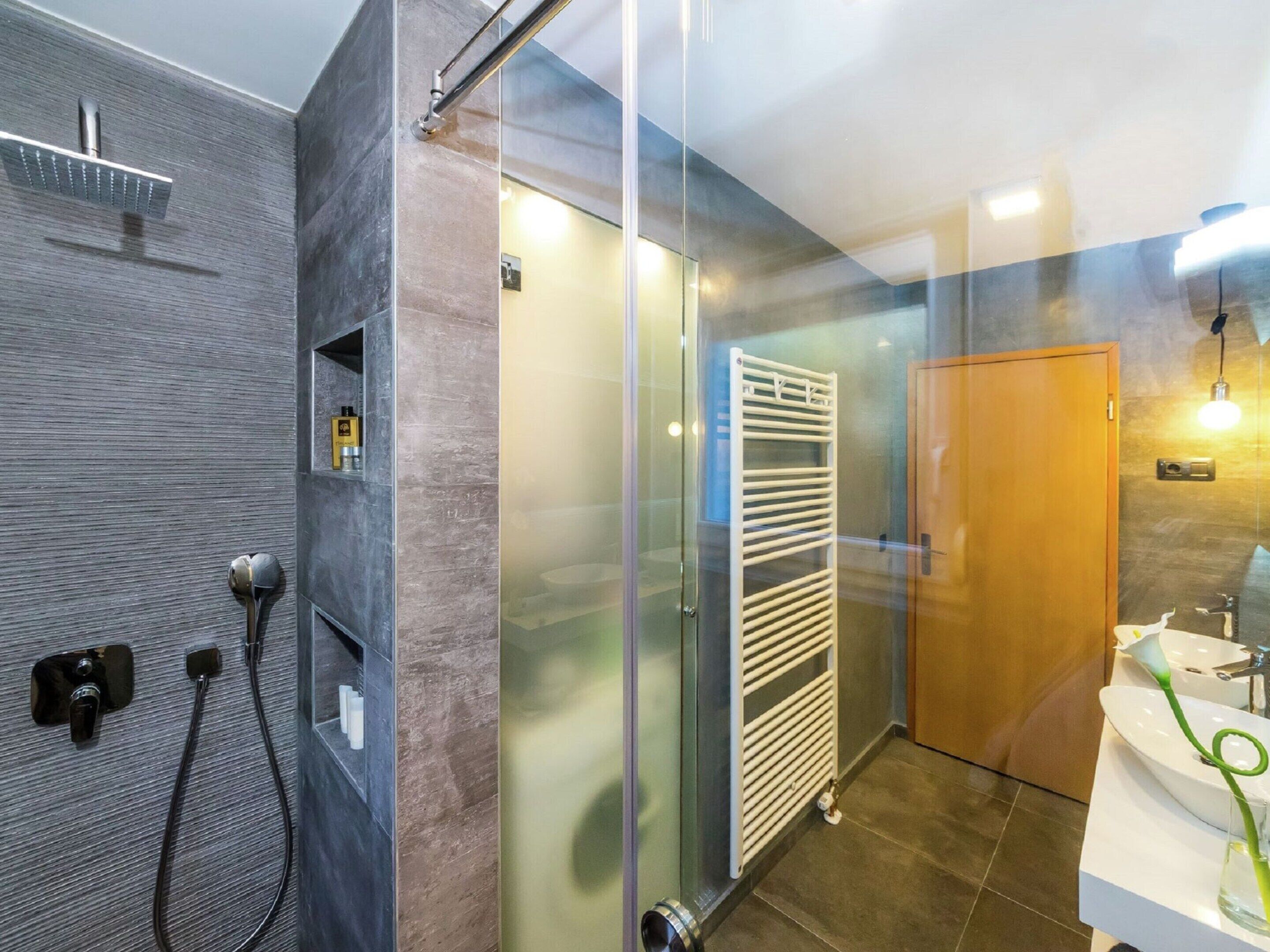 A modern bathroom with a glass shower enclosure, a white radiator, and a wooden door.