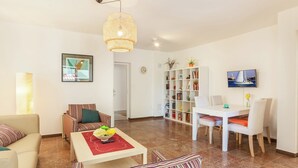 A living room with a sofa, a striped armchair, a coffee table with a bowl, a bookshelf, and a dining area with a table and chairs.