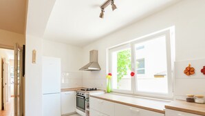A modern kitchen with white cabinets, a stove, oven, and a window with a view of greenery.