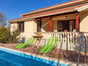 A poolside area with two green striped lounge chairs, a small table with a pitcher and glasses, and a railing.