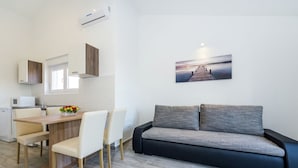 A modern kitchen with white cabinets, a wooden dining table, and a gray sofa.