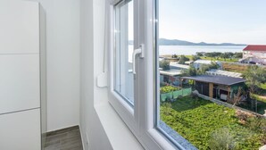 A modern apartment with a large window overlooking a green garden and a distant body of water.
