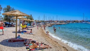 A beach with people sunbathing, umbrellas, and boats in the background.