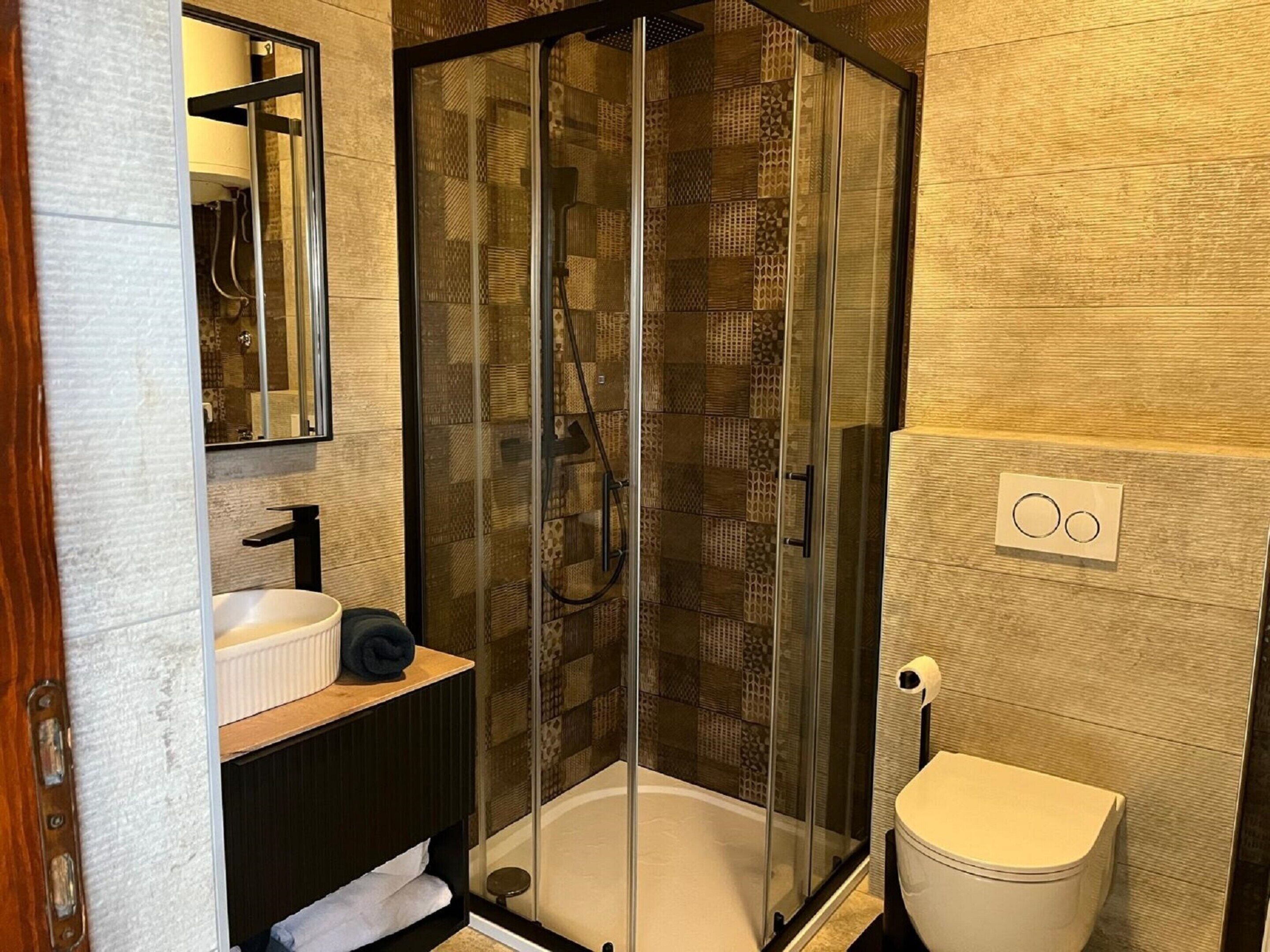 A modern bathroom with a glass-enclosed shower, a sink, and a toilet.