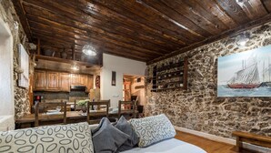 Una habitación acogedora con pared de piedra, techo de madera, zona de comedor y un cuadro de un velero.