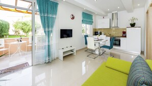 A modern living room with a green sofa, a dining area with a table and chairs, a kitchen with white cabinets, and a TV mounted on the wall. - Luxury Apartment in Zadar With Covered Terrace (Zadar)