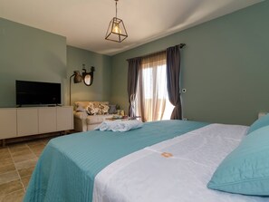 Un dormitorio con cama, televisión sobre un mueble, lámpara y ventana con cortinas.