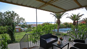 A covered outdoor seating area with a view of a swimming pool and greenery.