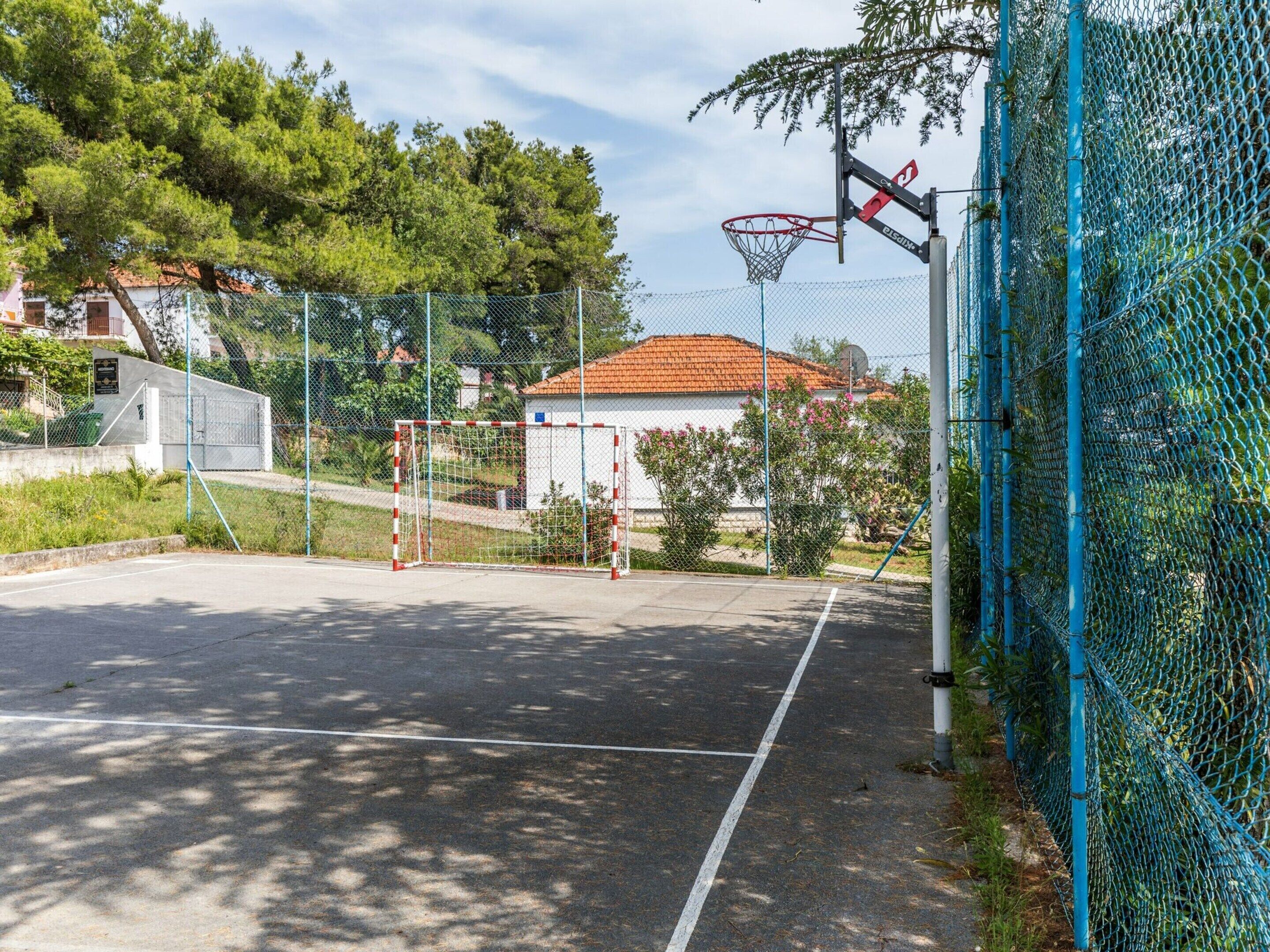 An outdoor basketball court with a chain-link fence, a basketball hoop, and a goal.