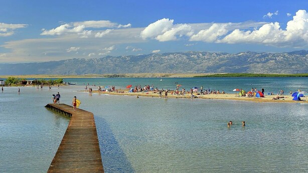 A beach with a wooden pier extending into calm waters, surrounded by mountains in the background. - Comfortable Apartment With Balcony in a Quiet Area, Near the Beach (Zadar)