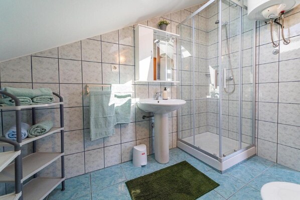 A bathroom with a glass shower enclosure, a white sink, and a shelf with folded towels.
