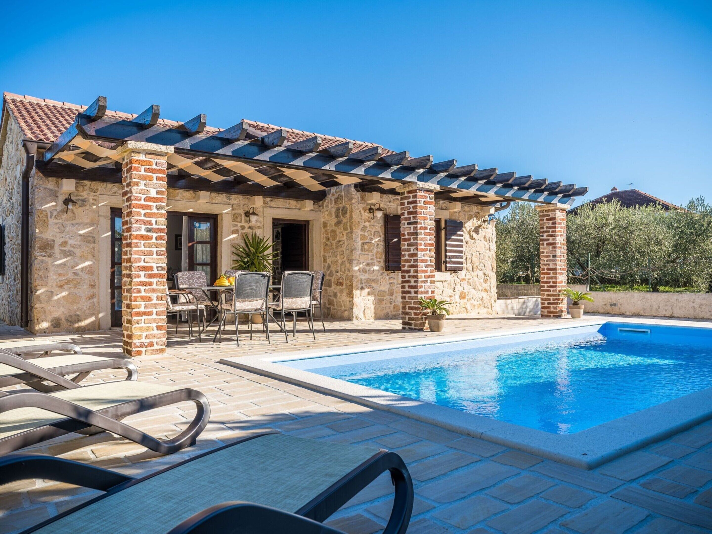 A stone building with a pool, outdoor seating, and a pergola.