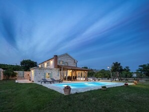 Une maison en pierre avec une piscine, un espace extérieur aménagé pour se détendre et une pelouse bien entretenue.