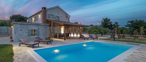 Una casa de piedra con piscina, mobiliario de exterior y un patio cubierto.