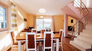 A dining area with a wooden table and chairs, a staircase with metal railings, and a view through large windows. - Spacious Holiday Home in Pakoštane near Sea (Pakostane)