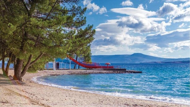 A beach with a red boat, clear blue water, and a mountainous background. - Spacious Holiday Home in Pakoštane near Sea (Pakostane)