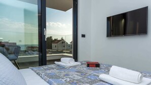 A hotel room with a bed, a TV, a glass door leading to an outdoor area, and a small table with a book. - Luxury Villa With Private Pool, Great sea View, Near the Beach (Pakostane)