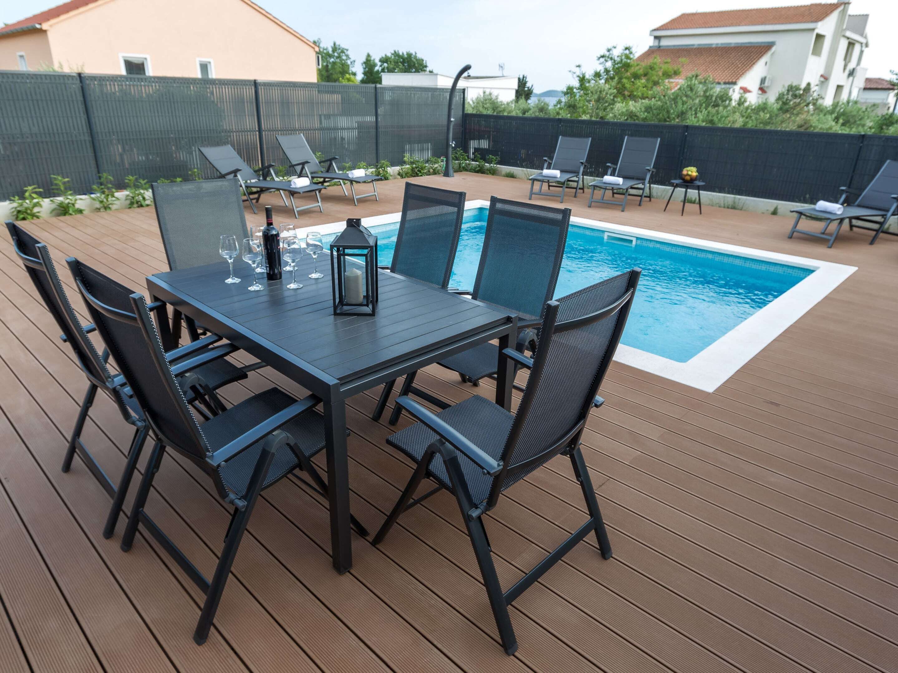 Een zwembadterras met een tafel, stoelen, een zwembad en een hek.