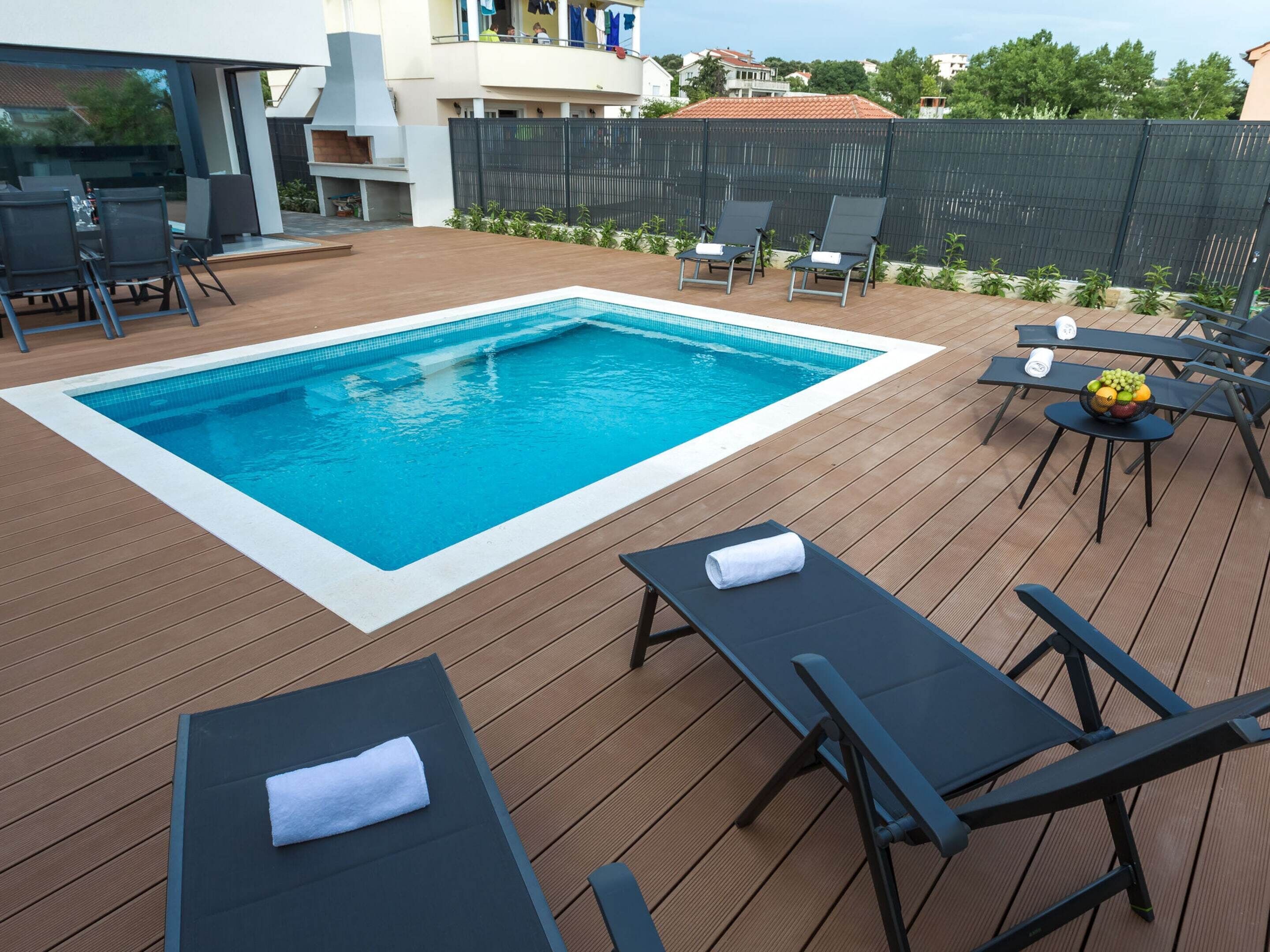 A swimming pool with lounge chairs and a table with fruit.