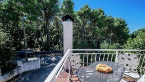 A balcony with a round table and chairs, a small birdhouse, and a view of a road and trees.