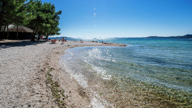 A beach with clear water, a few people, and trees.