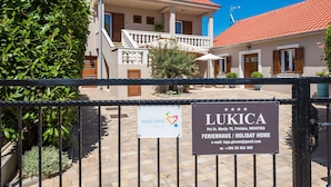 Uma casa de dois andares com telhado de telhas vermelhas, varanda e placa indicando ser uma casa de temporada chamada LUKICA.