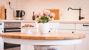 Uma cozinha com uma mesa redonda de madeira, armários brancos e um vaso branco com flores cor-de-rosa.