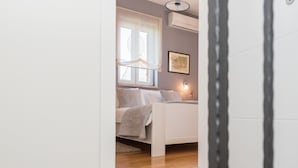 Quarto com cama, janela, aparelho de ar condicionado e um quadro na parede.