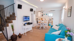 Uma sala de estar moderna com um sofá azul, uma mesa de jantar e uma cozinha ao fundo.