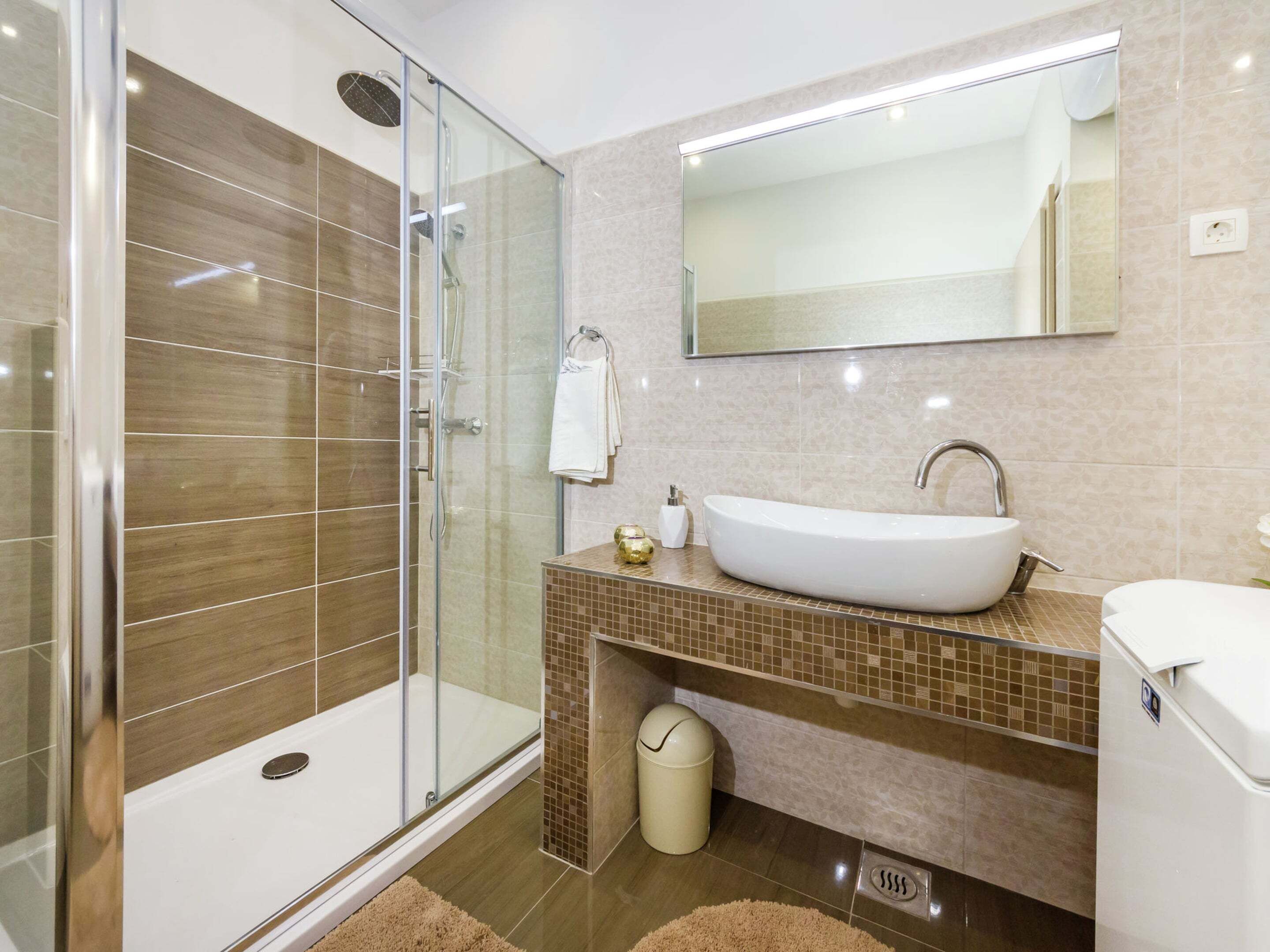 A modern bathroom with a glass-enclosed shower, a white sink, and a large mirror.