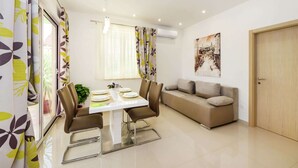 A modern living room with a dining area, featuring a sofa, a dining table with chairs, and a large window with curtains. - New Luxury Apartment With Nice Garden and Barbecue in a Quiet Area, Wifi (Zadar)