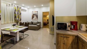 A modern kitchen with a microwave, coffee maker, and cabinets. There is a dining area with a table and chairs. - New Luxury Apartment With Nice Garden and Barbecue in a Quiet Area, Wifi (Zadar)