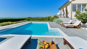 Une piscine avec des chaises longues et une table où sont disposés des fruits et des boissons.