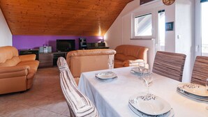 Uma sala de jantar com uma mesa posta para quatro pessoas, uma televisão ao fundo e teto de madeira.