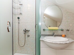 Et badeværelse med en brusekabine i glas, en vask med bordplade i marmor og et spejl over vasken.