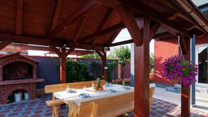 Um pátio externo com forno de tijolos, mesa de madeira e bancos.
