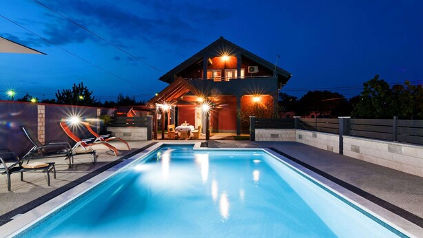 Uma casa moderna com piscina, área de estar ao ar livre e um pátio bem iluminado.