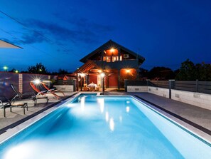 Et moderne hus med swimmingpool, udendørs møbler og en godt oplyst patio.