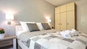 A neatly made bed with a quilt, bedside lamps, a nightstand with a plant, and a wardrobe. - Modern Holiday Home With Pool (Bibinje)