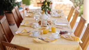Une table de petit-déjeuner dressée avec des assiettes, des tasses, un pichet de jus d’orange et un vase rempli de fleurs.