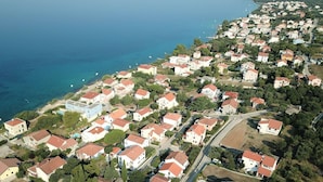 Vue aérienne d’une zone résidentielle côtière, avec des maisons, des routes et une mer bleue et limpide.